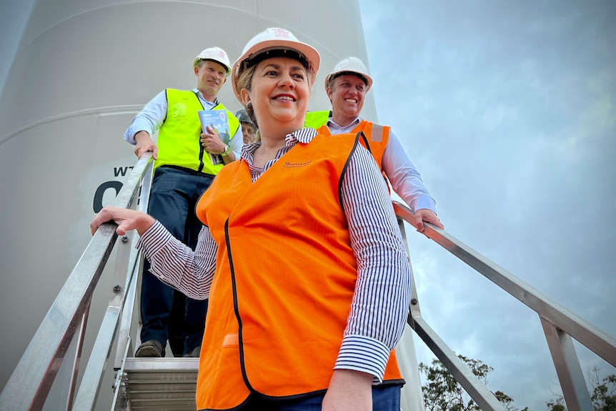 A smiling woman in high-vis and a hard hat – Queensland Premier Annastacia Palaszczuk – descends a flight of stairs/